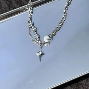 Detail of Y2K star pendant necklace with mixed chains on a silver metallic tray