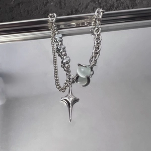 Macro detail of multi-layered silver star necklace with blue opal bead and cross pendant