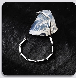 Dettaglio del bracciale a maglie geometriche argentate su un supporto di cristallo