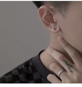 Gros plan d'une boucle d'oreille trèfle noir et d'une bague argentée sur un modèle