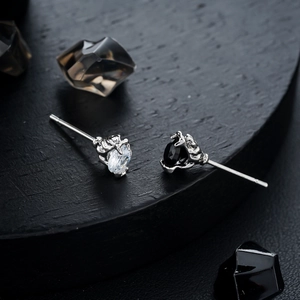 Gothic claw earrings featuring white zircon and black gemstone on a dark display stand