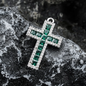 Macro d'un pendentif croix en argent avec zircons verts émeraude sur roche noire