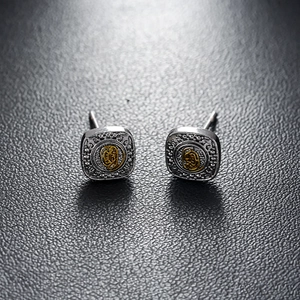 Vintage silver and gold square stud earrings with embossed texture on black leather