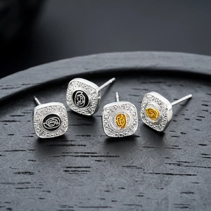 Square silver stud earrings with black and gold center logo and sparkling crystal border