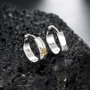 Polished silver hoop earrings with a gold sun spiral on dark volcanic rock background