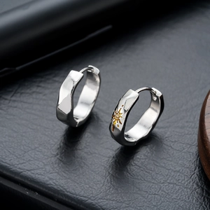 Silver hoop earrings with golden sun engraving on dark leather and wood background