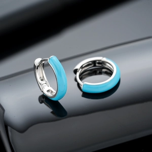 Modern light blue enamel huggie earrings with silver finish on reflective black background