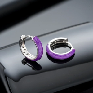 Detailed view of silver hoop earrings with purple enamel inlay on a black reflective surface