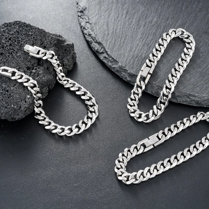 Three silver titanium steel Cuban chain bracelets displayed on volcanic black rock