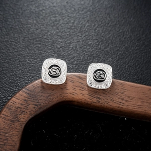 Macro shot of silver square stud earrings with black circular inlay and retro engraving