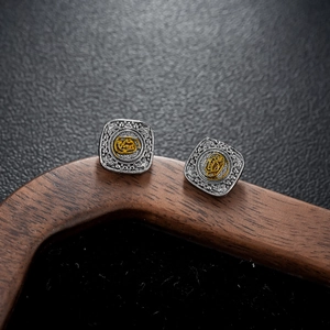 Macro detail of square vintage silver stud earrings with golden relief logo