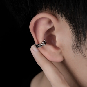 Vintage hollow cross ear cuff in silver metal worn on ear cartilage with black background