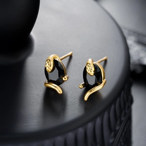 Gros plan de boucles d'oreilles serpent dorées avec une pierre noire facettée sur socle