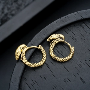 Close-up of golden snake hoop earrings with detailed texture on a dark wooden tray