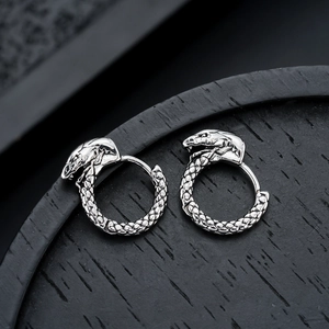 Macro detail of snake-shaped silver earrings with realistic scale texture on wood