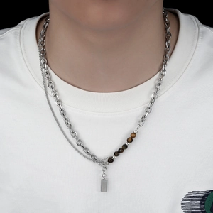 Detail of layered cuban chain necklace featuring tiger eye beads and rectangular metal pendant