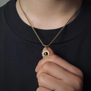 Goldene Sonnenstrahl-Halskette mit braunem Edelstein vor schwarzem T-Shirt-Hintergrund