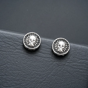 Macro shot of silver skull magnetic earrings with black zircons on leather texture