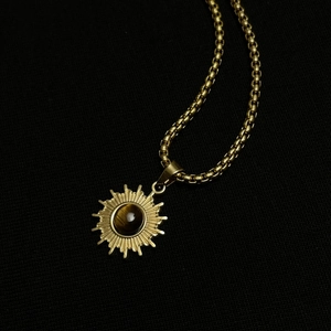 Goldene Sonnenanhänger-Halskette mit Tigerauge-Stein an einer Kette auf Schwarz