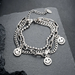 Detail of layered stainless steel chains with smiling face pendants on stone surface