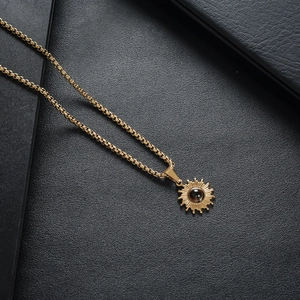 Detail der goldene Sonnenanhänger mit schwarzem Stein auf Boxkette vor Lederhintergrund