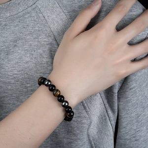 Men's natural obsidian and tiger eye beaded bracelet shown on a wrist over a grey fabric