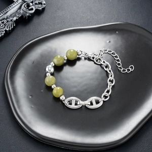 Detail of silver chain bracelet with green gemstones and anchor buckle on black tray