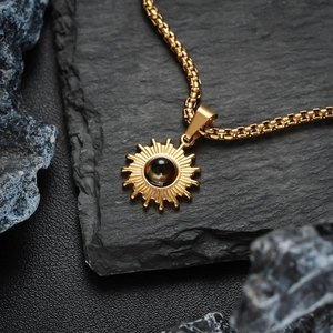 Detail der goldenen Sonnenanhänger-Halskette mit schwarzem Edelstein auf dunklem Stein