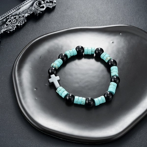 Macro view of cross pendant with turquoise and black beads on a ceramic tray