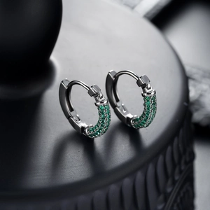 Macro detail of silver hoop earrings featuring micro-paved green zircon gemstones