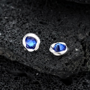 Silver Mobius magnetic earrings with blue cubic zirconia on black volcanic rock