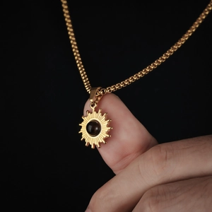 Makroaufnahme von Sonnenanhänger mit schwarzem Stein an einer goldenen Box-Halskette