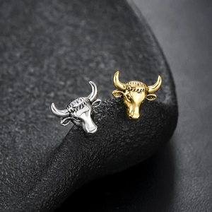Macro shot of ox head studs in gold and silver finish with detailed carvings on dark rock