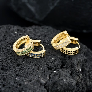 Macro shot of gold-plated hip hop earrings with multi-colored stones on volcanic rock