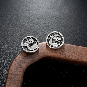 Macro detail of vintage silver reindeer stud earrings on a dark textured background