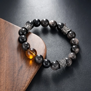 Obsidian beaded bracelet with amber accent bead and silver hollow spacers on dark background