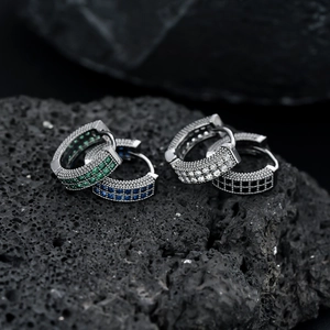 Macro view of iced-out huggie earrings with colorful zircons on black volcanic rock
