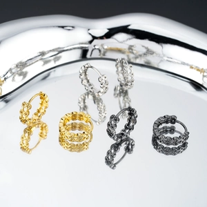 Macro detail of textured chain hoop earrings in gold, silver and black on metal tray