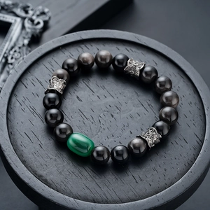 Macro shot of natural obsidian beads bracelet with green gemstone and carved silver spacers