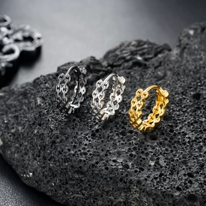 Close-up of punk style hollow chain earrings in black, silver, and gold on lava rock