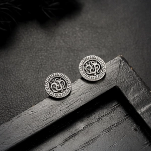 Close-up of vintage oxidized silver stud earrings with engraved fret pattern on black tray