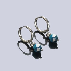 Détail de créoles argentées avec perles géométriques bleues facettées et design moderne