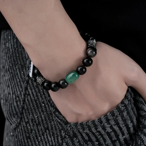 Close-up of a beaded natural obsidian bracelet with a green stone and silver spacers