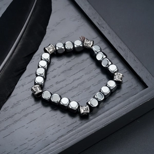 Detail of square hematite beads with intricate engravings and black feather decoration