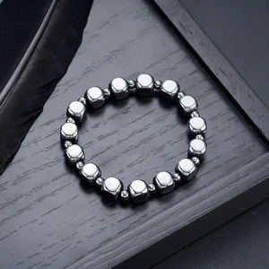Close-up of geometric cube hematite beads on a dark wooden tray with a black feather
