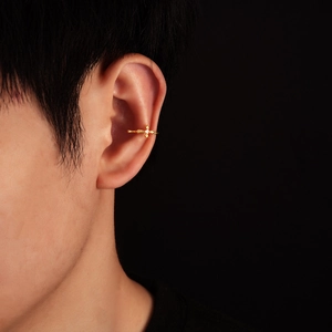 Close-up of a gold cross ear cuff with a sparkling white crystal on male model ear