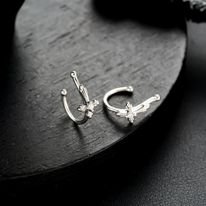 Detailed close-up of silver butterfly ear cuffs with small crystals on a dark wood base