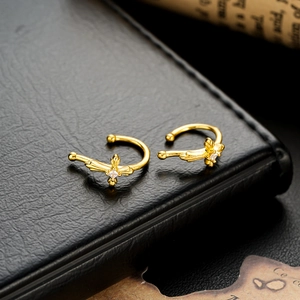 Macro detail of gold cross ear cuff with center zircon on a black leather background