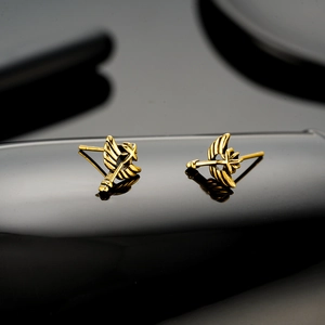 Golden angel wing earrings with sword design shown on a reflective black surface