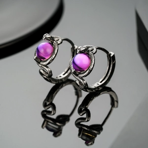 Dettaglio di orecchini a cerchio a serpente vintage con perla viola su superficie nera